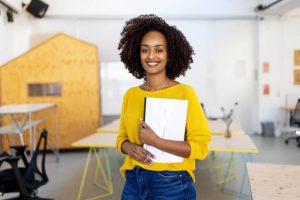 Portrait of a female business professional standing in office holding laptop. Confident business executive in office looking at camera